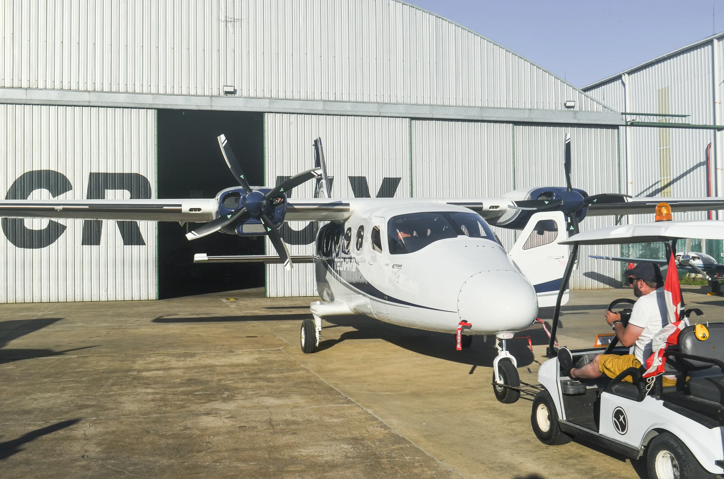 Twin-engine aircraft in front of the hangar, ready to operate